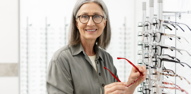 Smiling woman choosing red glasses from an eyewear display