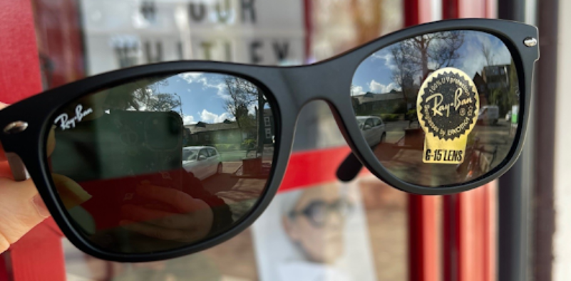 A close up of a person holding a pair of black Ray-Ban sunglasses.
