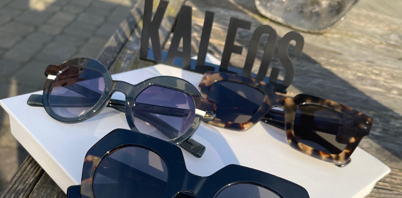 A selection of Kaleos sunglasses on a white block, with a metal ‘KALEOS’ logo positioned behind them