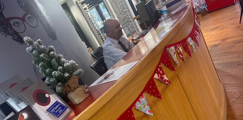 A photo of the interior of Robinson Optometrists with a person sat at the reception desk which has been decorated with a mini Christmas tree and festive bunting.