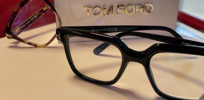 A close-up of a pair of black Tom Ford glasses, in front of Tom Ford branded point of sale.