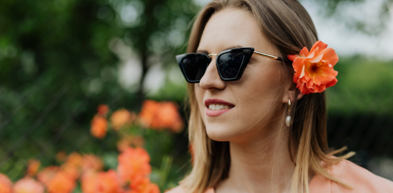 A woman wearing cat-eye style sunglasses with an orange flower tucked behind her ear.