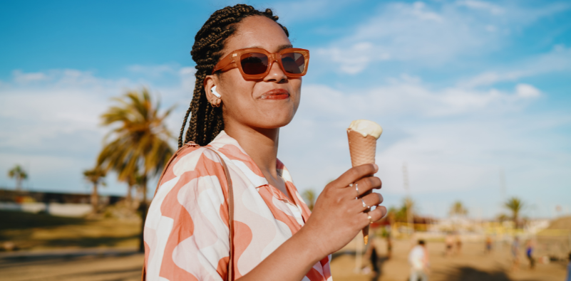 Woman wearing brown sunglasses and holding an ice cream outdoors.