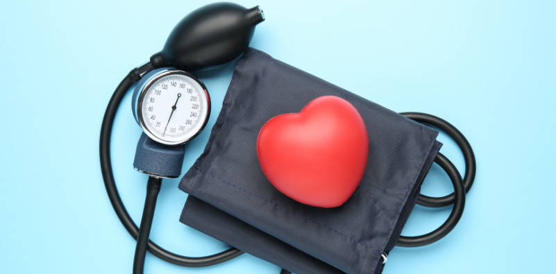 A blood pressure cuff on a blue background with a red heart resting on top of the cuff.