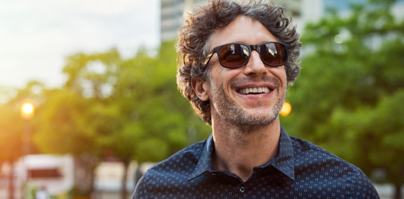 A man outside, smiling, while wearing glasses with brown tinted lenses.