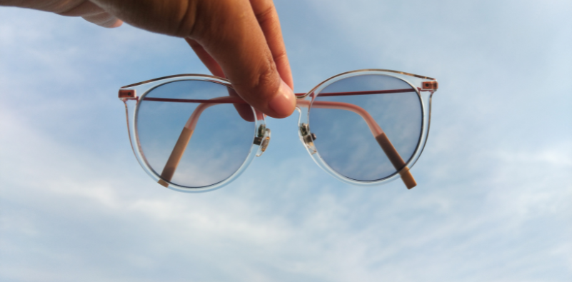 A person holding a pair of glasses with photochromic lenses against the sky.