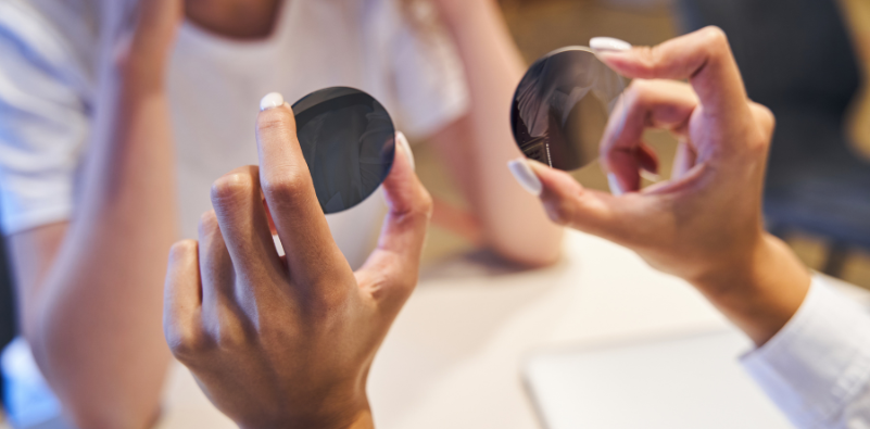 An optician holding up two spectacle lenses for a patient.