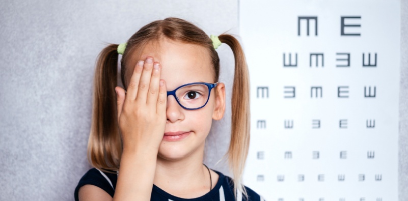 A young girl wearing glasses covering one eye with her hand at the opticians