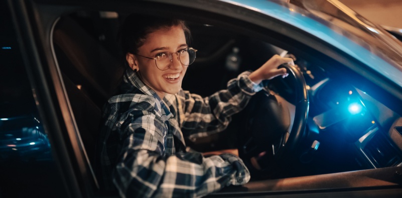 A woman wearing a pair of glasses, driving her car at night.