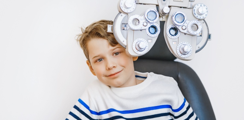A young school boy sat behind the phoropter at the optician's, ready for an eye test.