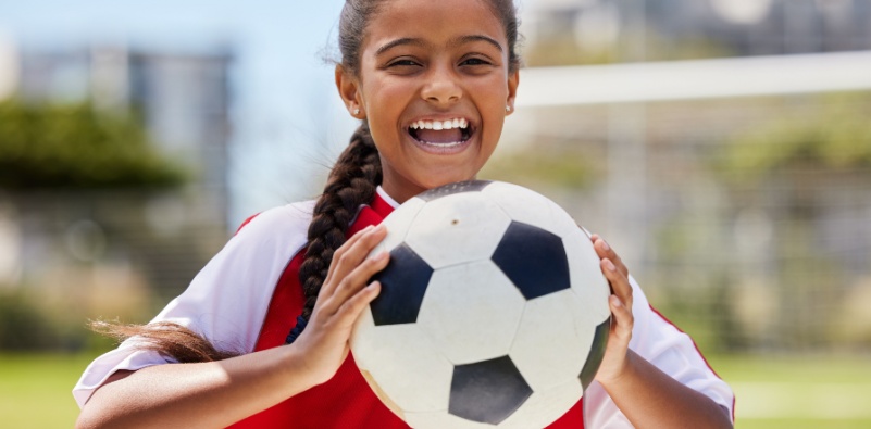 A happy Indian girl holding a football on a field