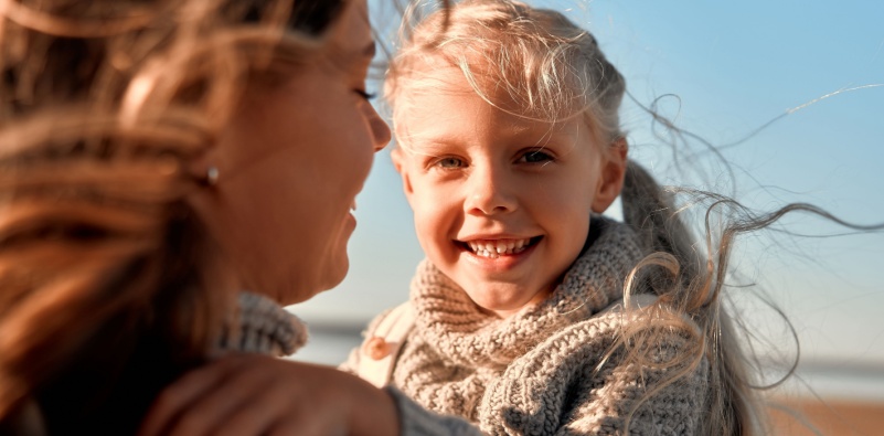 An image of a child smiling outdoors with her mum