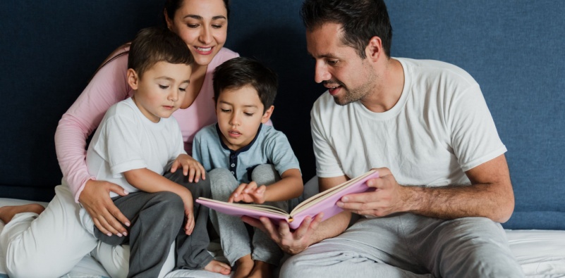 A mother and father reading a book to their two young boys.