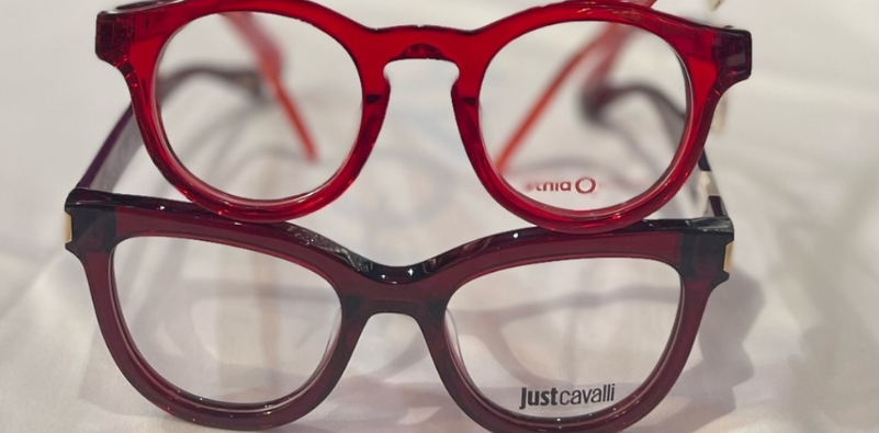 Two pairs of round-frame glasses, one red and one burgundy, stacked on top of each other on a white surface.